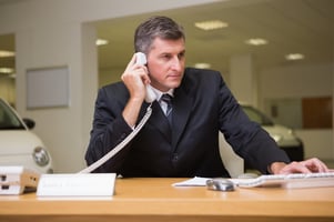 Focused businessman using laptop on the phone at new car showroom