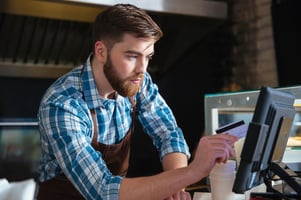Handsome concentrated bearded waiter swiping credit card through the computer terminal in cafe-1